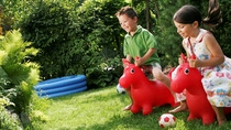 Two young kids ridding red plastic blow-up horses on a green lawn. Two young kids ridding red plastic blow-up horses on a green lawn.