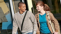 A young couple exiting a train, smiling at each other.