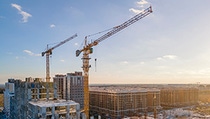 Construction cranes against a blue sky and city background. Construction cranes against a blue sky and city background.