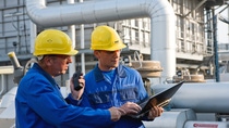 Two workers in overalls and helmets in front of a production plant