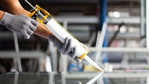 A man applying adhesives on a glass window pane. A man applying adhesives on a glass window pane.