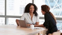 Two women sitting at a table with a notebook computer, talking and smiling. Two women sitting at a table with a notebook computer, talking and smiling.
