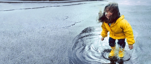 Girl (3-5) jumping in puddle wearing rain gear