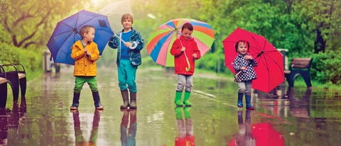 Four young children with colorful umbrellas playing in the rain