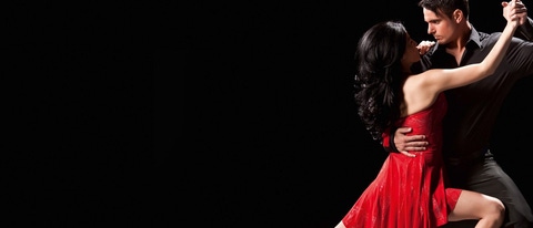 A couple dancing the tango against a black background. The man is wearing a black suit, the woman a red dress A couple dancing the tango against a black background. The man is wearing a black suit, the woman a red dress